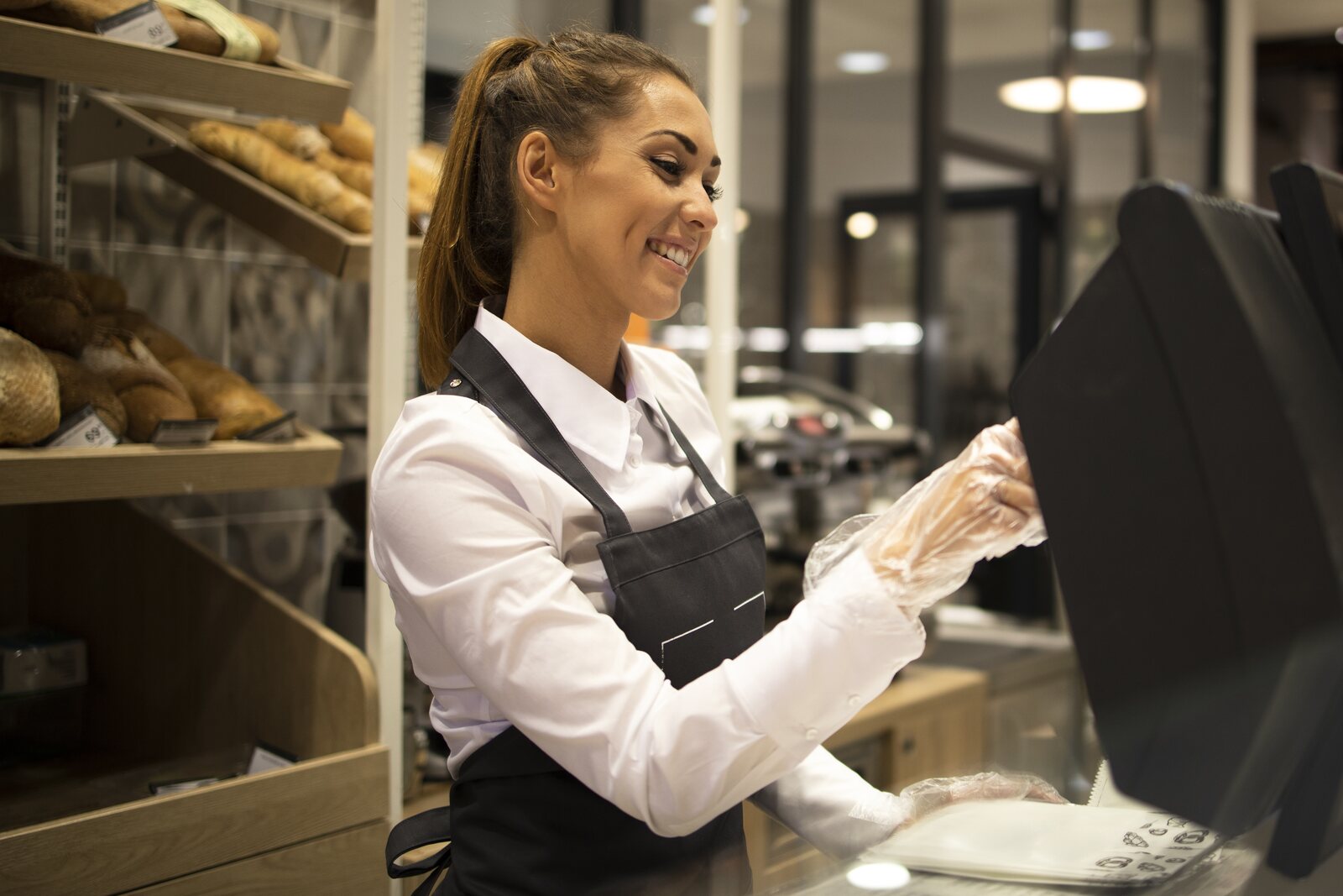 Addetta di una panetteria, con guanti monouso, al banco di vendita degli alimenti