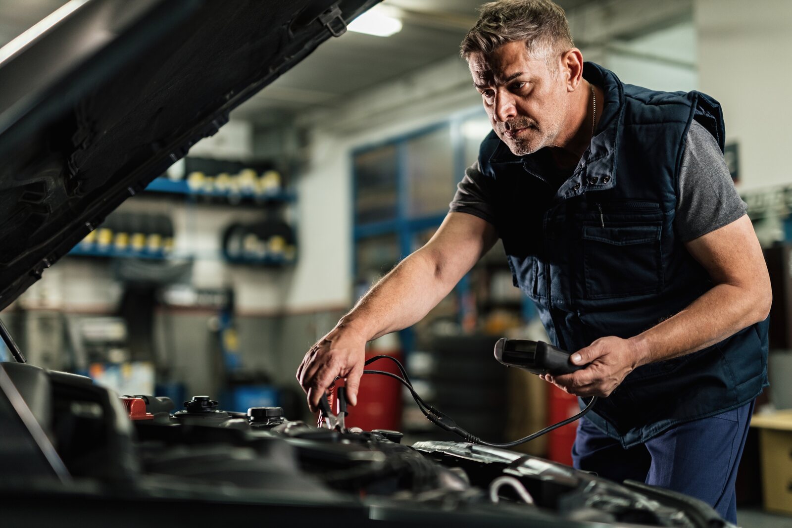 Meccanico al lavoro sul vano motore di un'auto in officina, con uno strumento diagnostico in mano